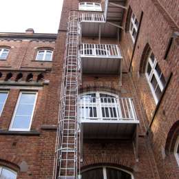 3 verdiepingen brandladder met kooi en toegangsbalkons op elk niveau van een fabrieksgebouw.