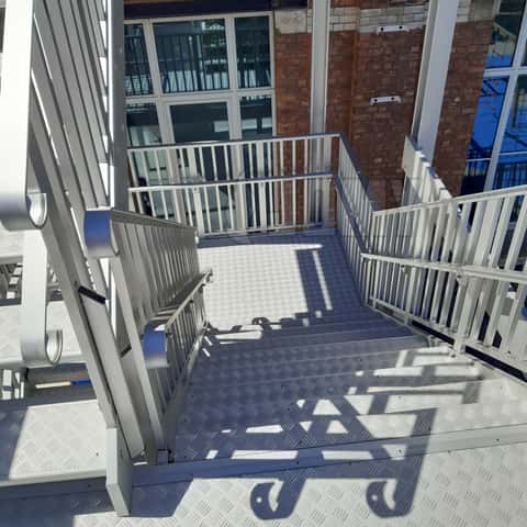 Mains courantes pour enfants et adultes, placées sur le même escalier d'évacuation.