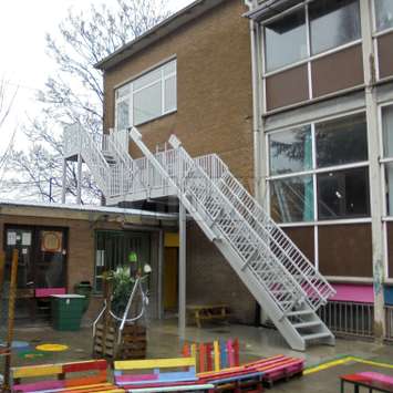 Fire escape stairs with a retractable flight installed in a school courtyard.